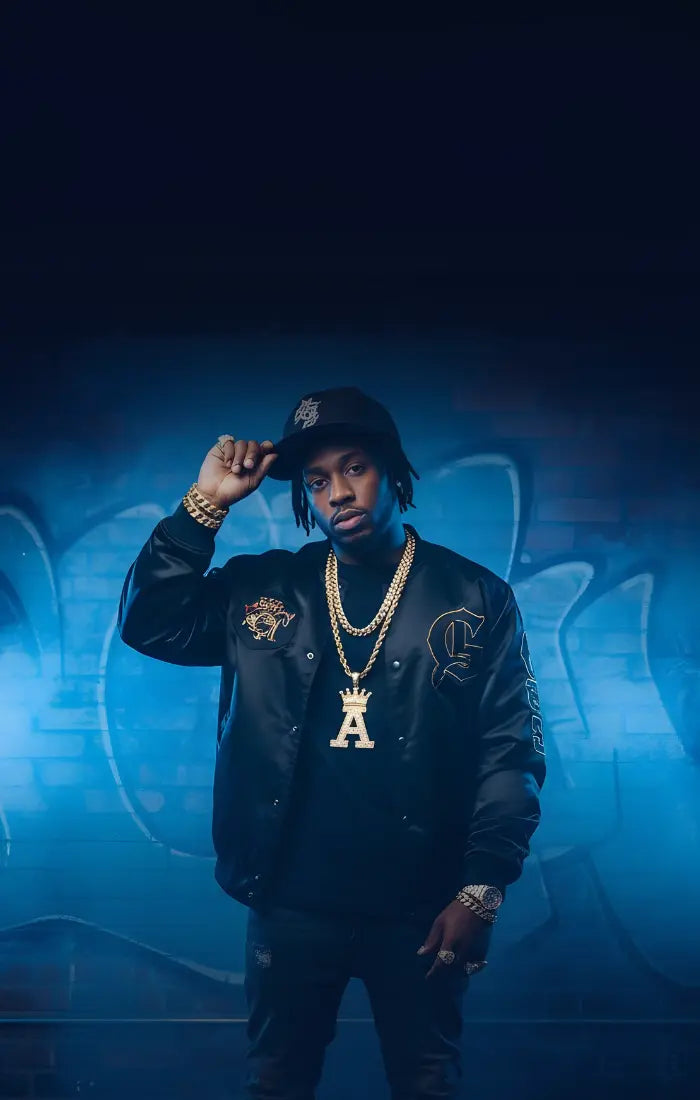 Person wearing a black jacket with gold accents and a gold chain, standing against a dark background.